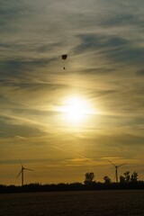 Vertical shot of a paraglider and wind turbines against the sunset sky