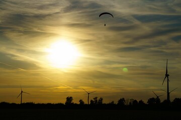 Fototapeta na wymiar Silhouette of a paraglider and wind turbines against the sunset sky