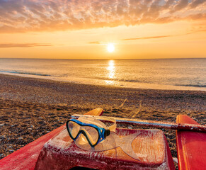 beautiful cloudy morning landscape with diving mask on a red old boat on foreground, sand beach, blue sea with surf and waves and cloudy sunset or sunrise on background