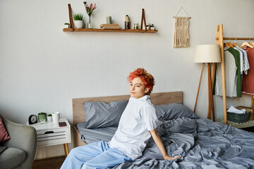 good looking extravagant person in white t shirt with red hair sitting on her bed, leisure time