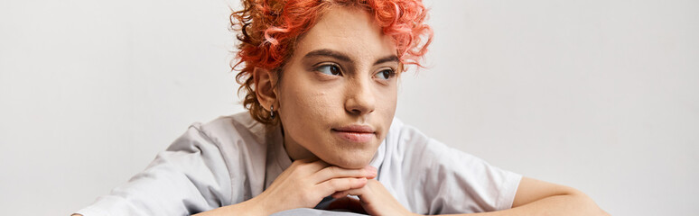 relaxing red haired queer person sitting on her bed at home and looking away, leisure time, banner