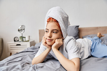 joyful beautiful queer person in homewear with hair towel chilling in her bed and looking away