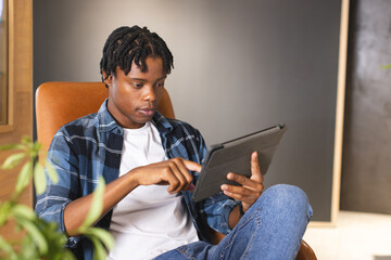 A young African American male using a tablet while sitting in a modern business office