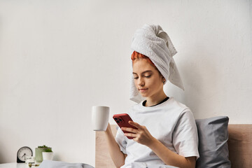 positive relaxing queer person in homewear with hair towel using phone and drinking tea in bed