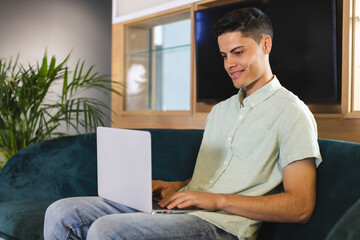 Biracial young man using laptop on blue sofa in a modern business office