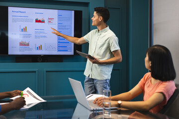 Biracial man presenting to diverse group in a modern business office, Asian woman listening
