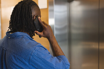 A young African American male is talking on a smartphone in a modern business office - 785147751