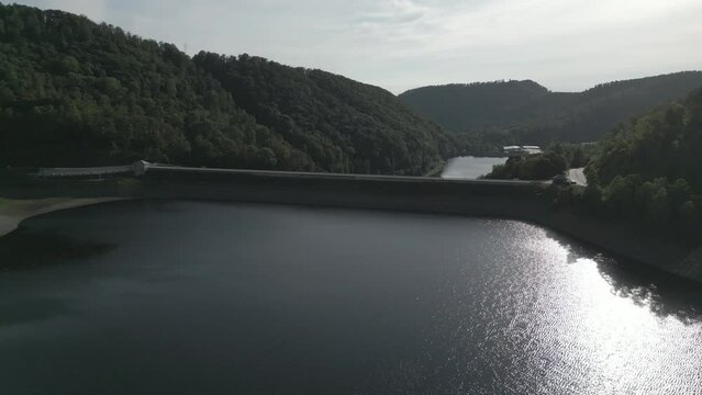 Aerial of a big water dum surrounded by the green hills with people walking on the bridge