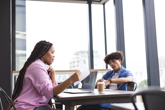A young biracial woman and man are working together in a modern business office, holding a tablet