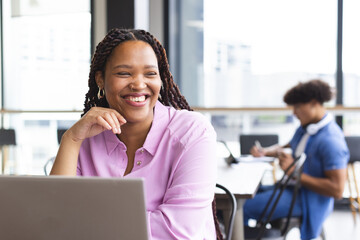 Biracial young woman with braided hair working on laptop, smiling