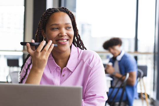 Young biracial woman talking on smartphone, working on laptop in a modern business office