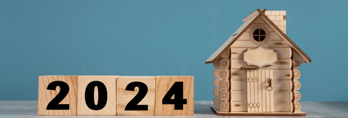Decorative wooden cabin and wooden cubes with 2024 inscription on blue studio background. concept...
