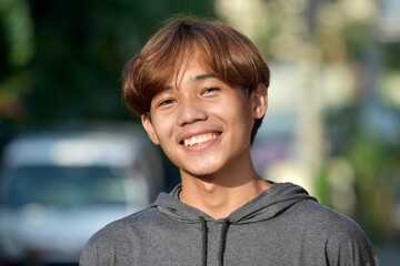 Portrait of a smiling teenage Southeast Asian boy with brown hair in the street
