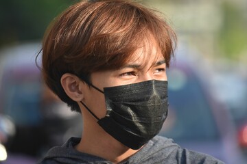 Portrait of a teenage Southeast Asian with brown hair wearing a black mask outdoors