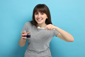 Young woman with mouthwash and toothbrush on light blue background