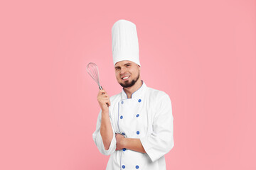 Happy professional confectioner in uniform holding whisk on pink background