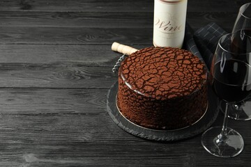 Delicious chocolate truffle cake, red wine and corkscrew on black wooden table, space for text