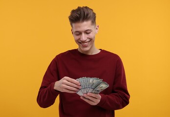 Happy man with dollar banknotes on yellow background