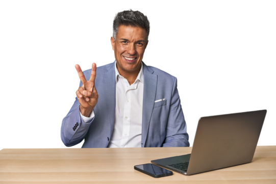 Elegant businessman at desk with laptop showing victory sign and smiling broadly.