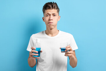 Young man using mouthwash on light blue background