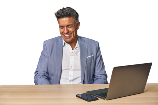 Elegant businessman at desk with laptop laughs and closes eyes, feels relaxed and happy.