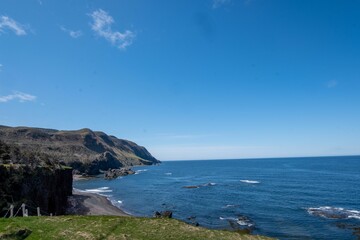 Scenic landscape with lush green vegetation and steep rocky cliffs on shore in Newfoundland, Canada