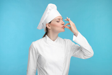 Woman chef in uniform showing perfect sign on light blue background