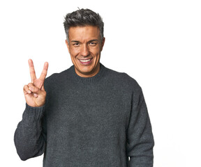 Middle-aged Latino man joyful and carefree showing a peace symbol with fingers.
