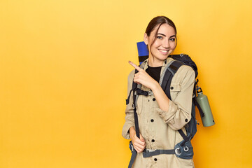 Explorer with mountain backpack ready smiling and pointing aside, showing something at blank space.