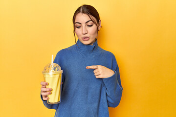 Young caucasian woman enjoying a creamy vanilla shake pointing to the side