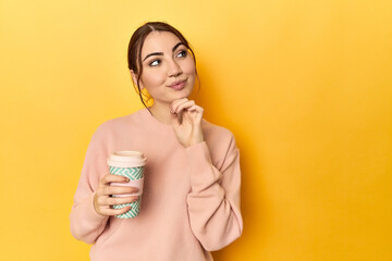 Young caucasian woman holding a takeaway coffee cup looking sideways with doubtful and skeptical...