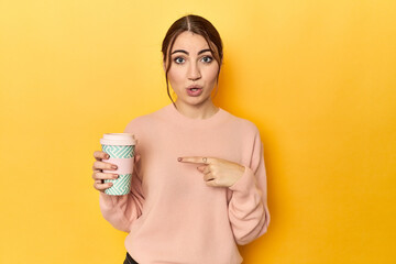 Young caucasian woman holding a takeaway coffee cup pointing to the side