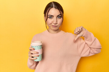 Young caucasian woman holding a takeaway coffee cup showing a dislike gesture, thumbs down....