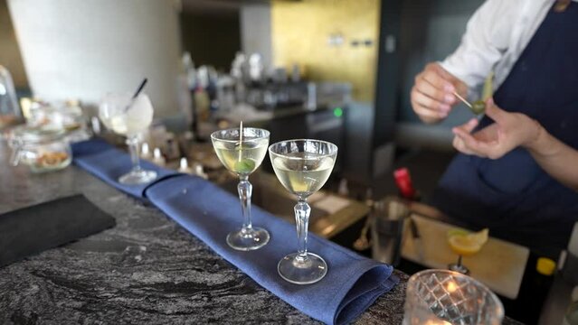 Slow-motion of skilled bartender mixing a glass of martini with a stick with green olive