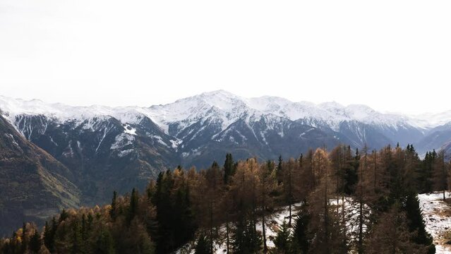 Beautiful view of a high and peaky mountain with snow on top in the background of a forest in autumn