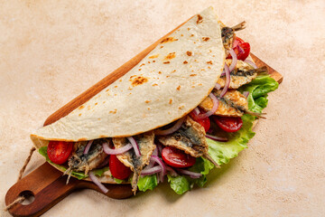 Traditional italian wrap or open sandwich. Piadina romagnola con sarde fritte. Fatbread with fried sardines fish, tomatoes, red onion and lettuce. Street food.