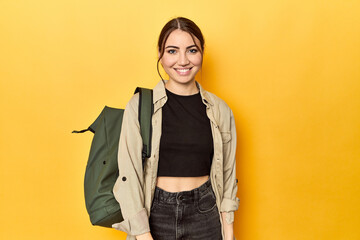 Young Caucasian woman with travel backpack on yellow
