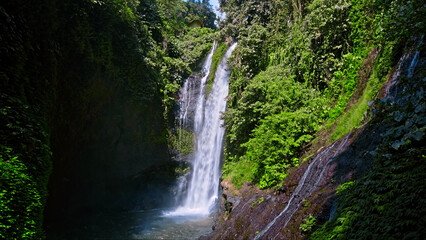 waterfall with rocks among tropical jungle with green plants and trees and water falling down