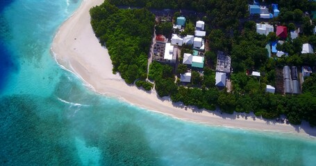 Aerial top view of houses surrounded with trees on the sandy beach near turquoise water in Maldives