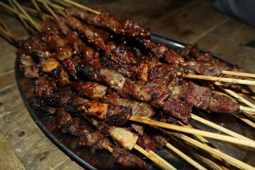 Close-up goat satay (Sate Kambing) served with green chili and sweet soy sauce, on a round white plate. Traditional cuisine of Indonesia.