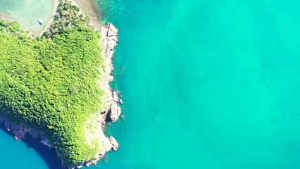 Aerial top view of an island covered with greenery against a turquoise sea