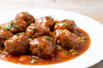 Meatballs, green peas and carrot with tomato sauce on wooden table. Close up