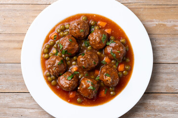 Meatballs, green peas and carrot with tomato sauce on wooden table. Top view