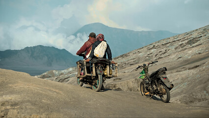 Two Indonesian people on a motorcycle ride through a volcanic desert