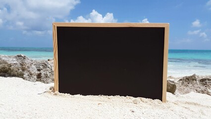 Closeup of a blackboard on a sandy beach against a turquoise sea