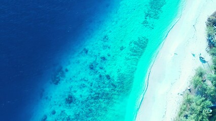 Aerial shot of  coral reefs under tranquil water in the sea and a whtie sandy beach