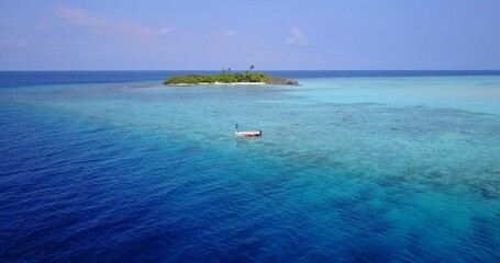 Aerial scenic view of turquoise water with coral reef and boat far from an island in the Maldives