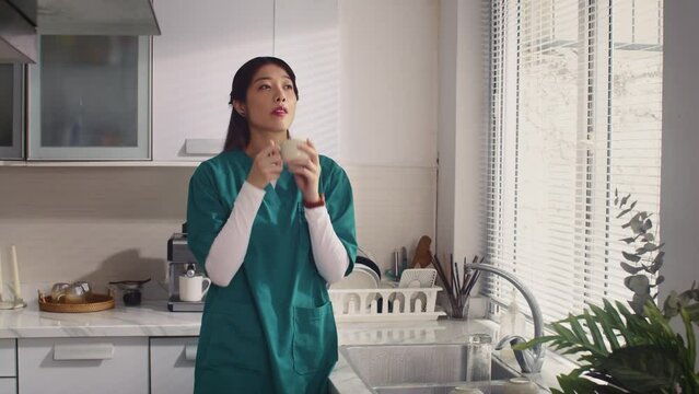 Copy space shot of Asian nurse in medical uniform drinking cup of morning coffee for breakfast at home kitchen