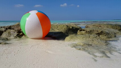 Closeup shot of a beach ball on the rocky coastline with the clear blue ocean in the horizon