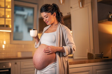 A beautiful pregnant woman caressing her belly and enjoying a cup of morning coffee in the kitchen